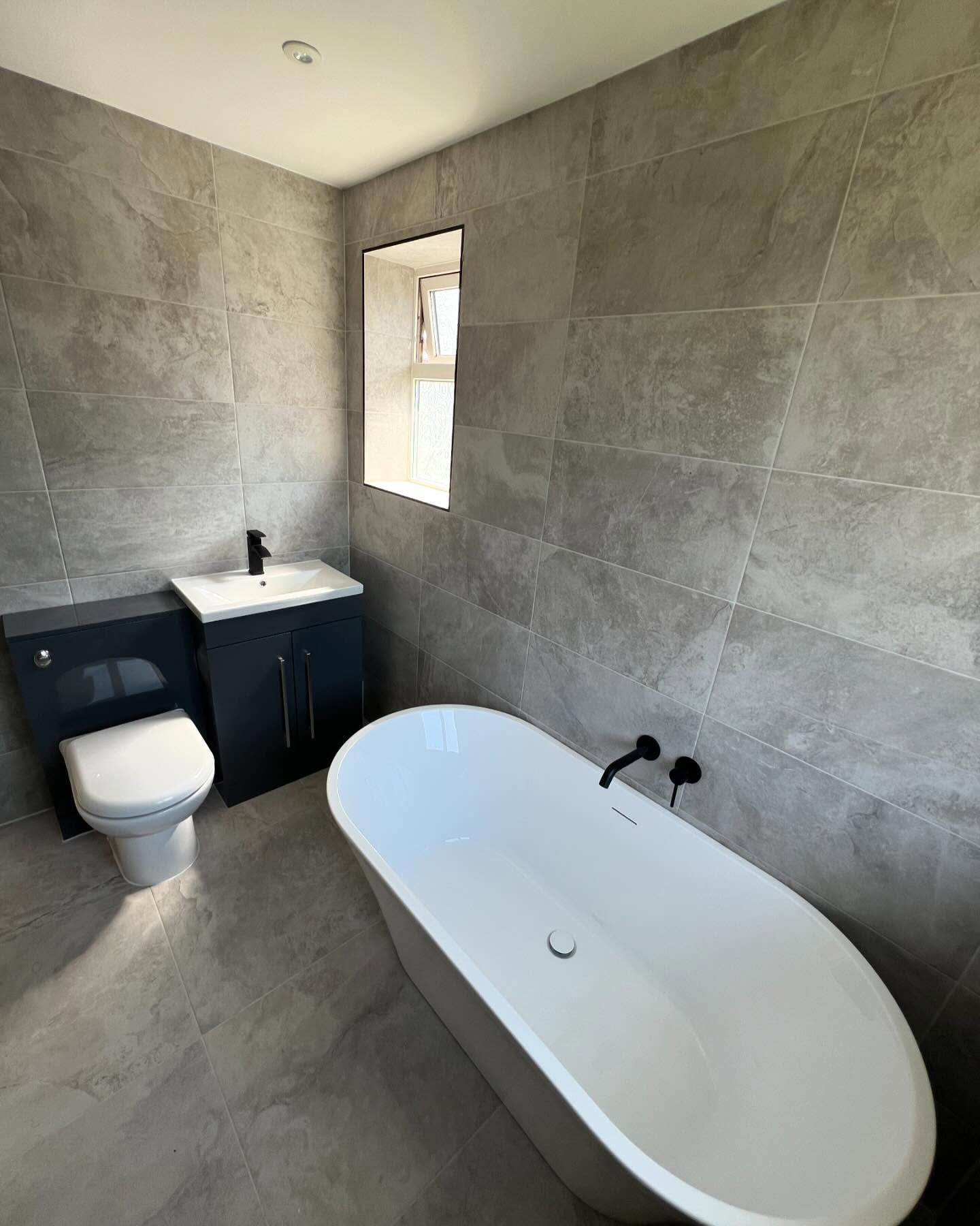 Freestanding bath against grey marble-effect tiled wall in new bathroom