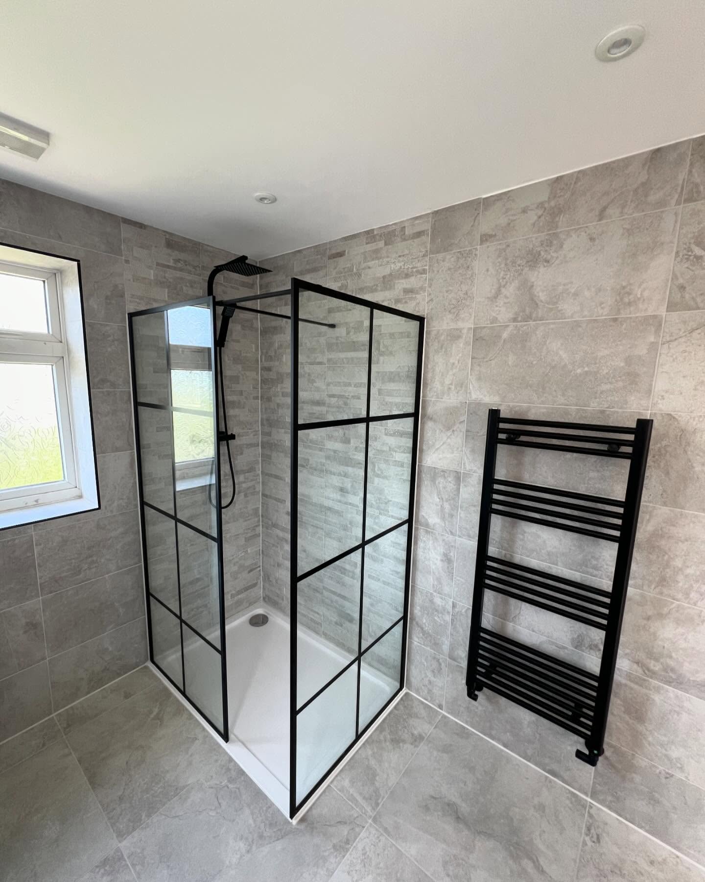 Walk-in shower enclosure with black heated towel rail in refurbished bathroom